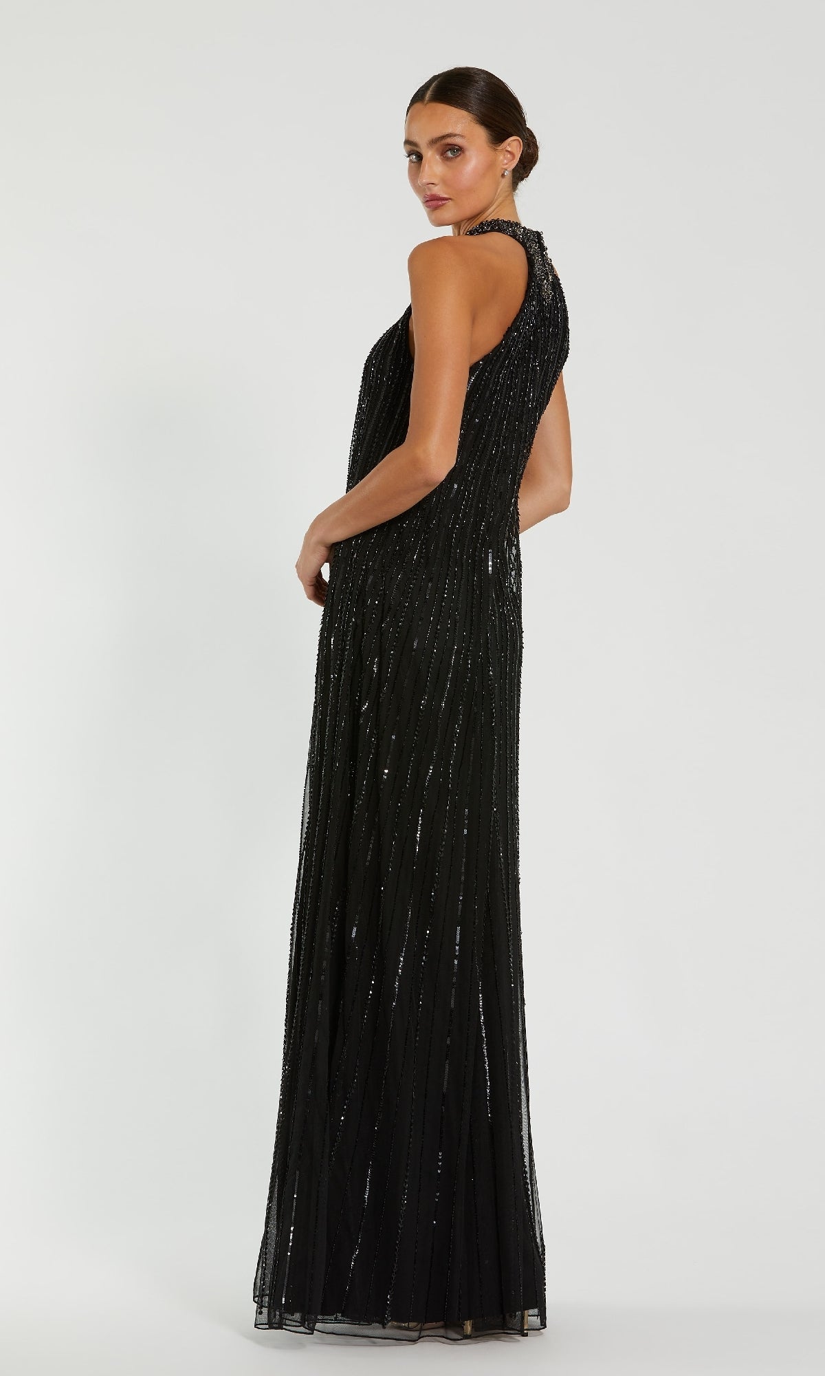A woman in the Mac Duggal 23043 long formal dress, featuring shimmering vertical embellishments and a sleeveless design, stands sideways against a plain light background.